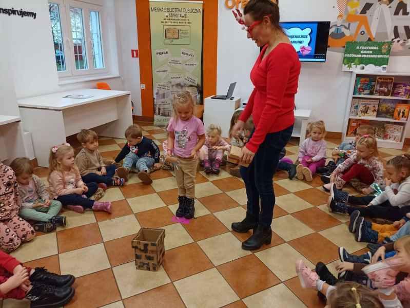 zdjęcie bibliotekarki obok dziewczynki rzucającej upominek do kartnowego komina w otoczeniu dzieci