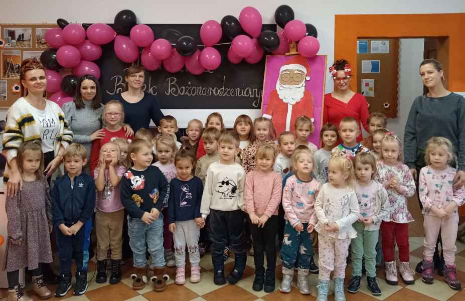 zdjęcie przedszkolaków, opiekunek grupy i bibliotekarki z obrazem mikołaja na stelażu