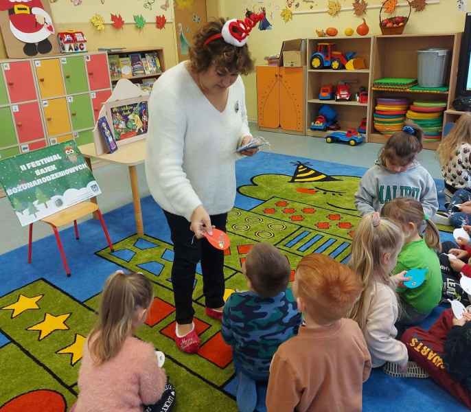 zdjęcie bibliotekarki rozdającej dzieciom na dywanie papierowe ozdoby świąteczne