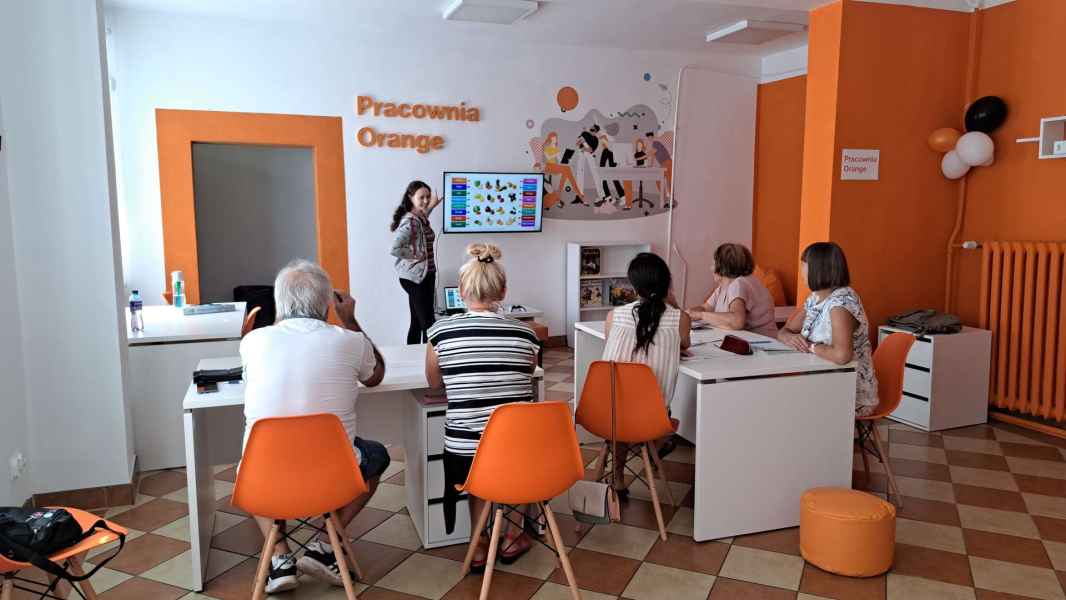 zdjęcie bibliotekarki i seniorów w trakcie lekcji j. angielskiego z użyciem ekranu telewizora