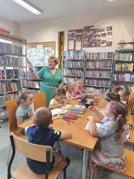 zdjęcie wychowawczyni i przedszkolaków oglądających książki w bibliotece