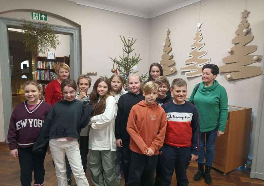 zdjęcie młodzieży z bibliotekarkami i wychowawczynią w holu biblioteki na tle udekorowanej choinki