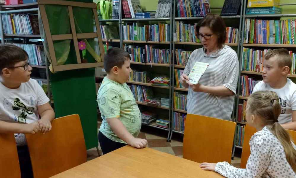 zdjęcie bibliotekarki wyjaśniającej grupie dzieci zasady wypożyczania zbiorów