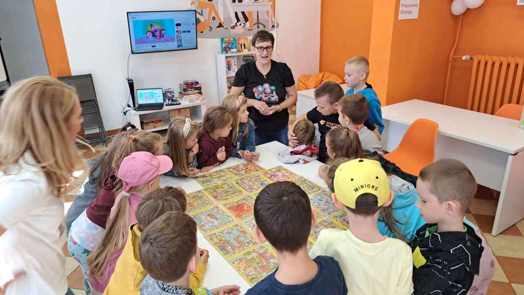 zdjęcie bibliotekarki tłumaczącej dzieciom zasady gry  przy stoliku