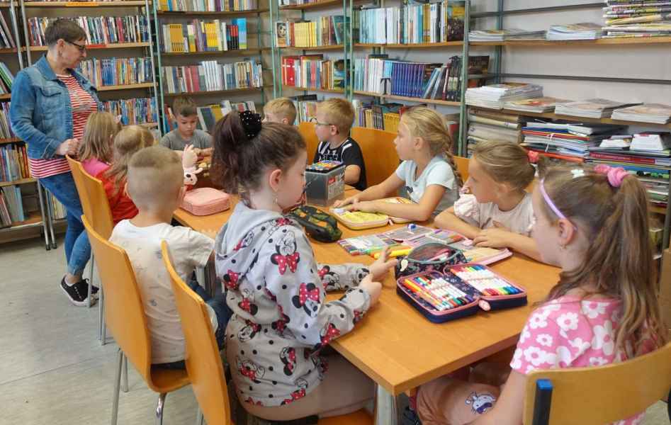 zdjęcie bibliotekarki tłumaczącej dzieciom zadanie do wykonania