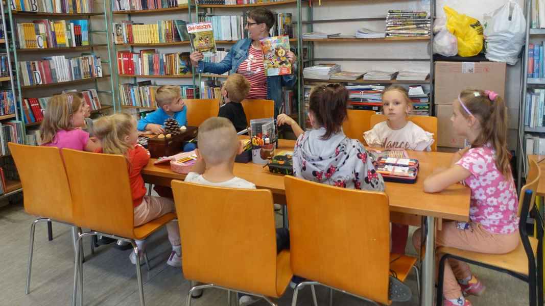 zdjęcie bibliotekarki omawiającej trzymane książki dzieciom