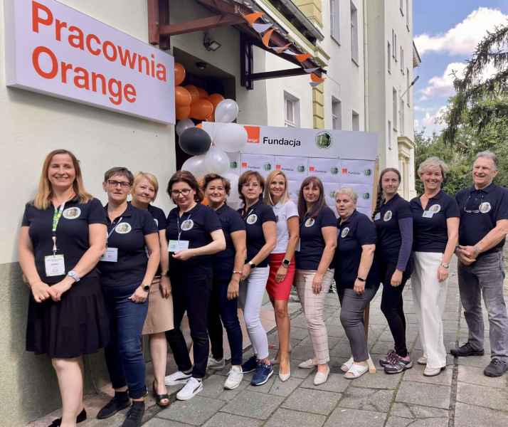 zdjęcie grupowe pracowników biblioteki na tle baneru z logo biblioteki i fundacji Orange