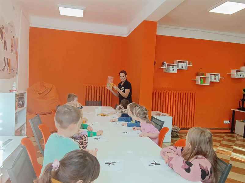 zdjęcie bibliotekarki pokazującej dzieciom przy stoliku książkę