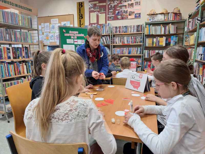 zdjęcie bibliotekarki pomagającej dzieciom w tworzeniu kotylionów