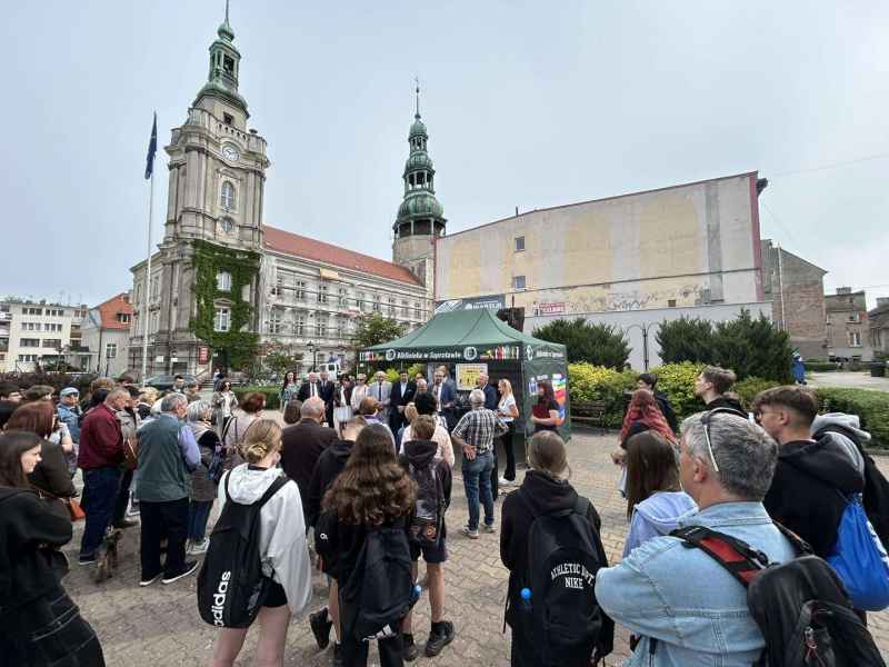 zdjęcie uczestników gry miejskiej na placu przed ratuszem słuchających burmistrza podczas otwarcia gry miejskiej