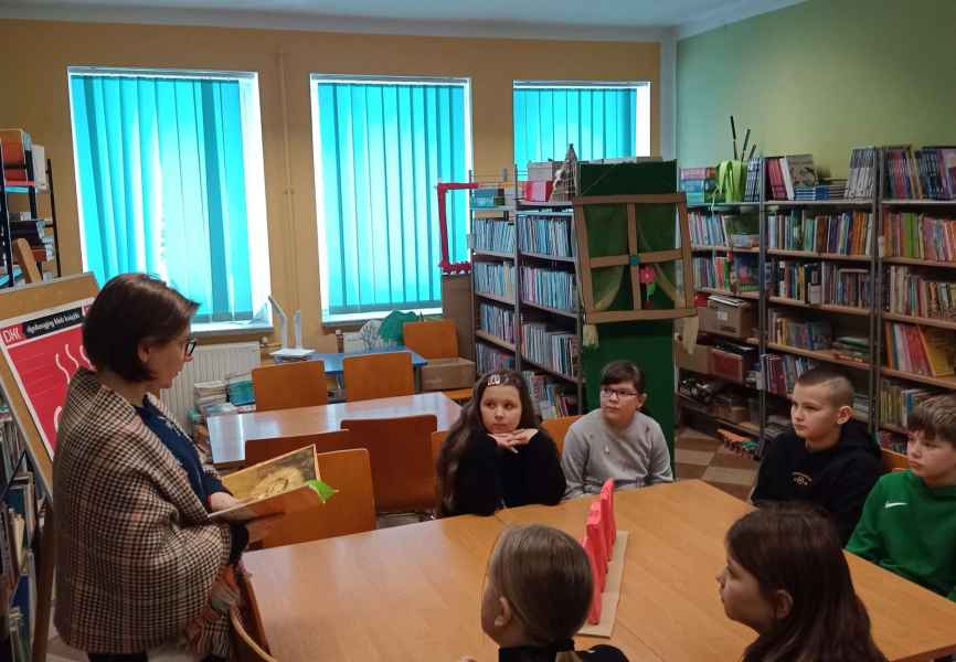 zdjęcie bibliotrekarki czytającej dzieciom siedzącym przy stoliku 