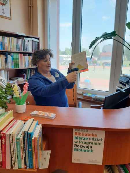 zdjęcie bibliotekarki pokazującej dzieciom skanowanie kodu książki