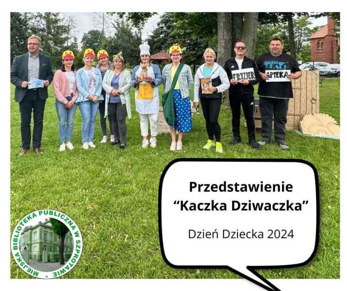 zdjęcie grupowe burmisrza, bibliotekarki i nauczycieli z rekwizytami na trawie, na dole napis przedstawienie kaczka dziwaczka dzień dziecka 2024, po lewej logo biblioteki