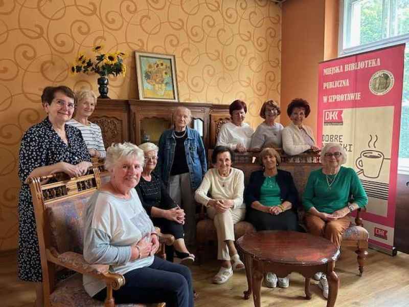 zdjęcie czytelniczek z książkami siedzących na fotelach i stojących przy banerze DKK
