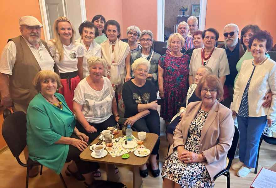 grupowe zdjęcie seniorów, dyrektor biblioteki oraz bibliotekarek dookoła stolika