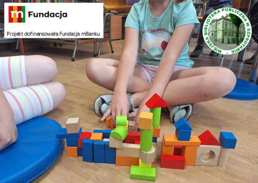 zdjęcie dzieci przy budowli z klocków na podłodze, na górze logo biblioteki i  mFundacji z napisem projekt dofinansowała Fundacja mBanku