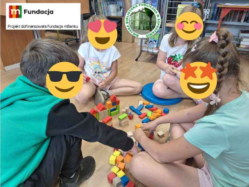 zdjęcie dzieci z zasłoniętymi emotikonami buziami na podłodze podczas układania klocków, na górze logo biblioteki i mFundacji z napisem Projekt dofinansowała Fundacja mbanku