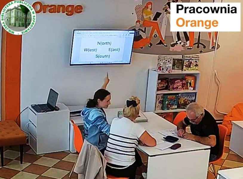zdjęcie bibliotekarki i kursantów podczas nauki angielskiego, na górze logo biblioteki i pracowni orange