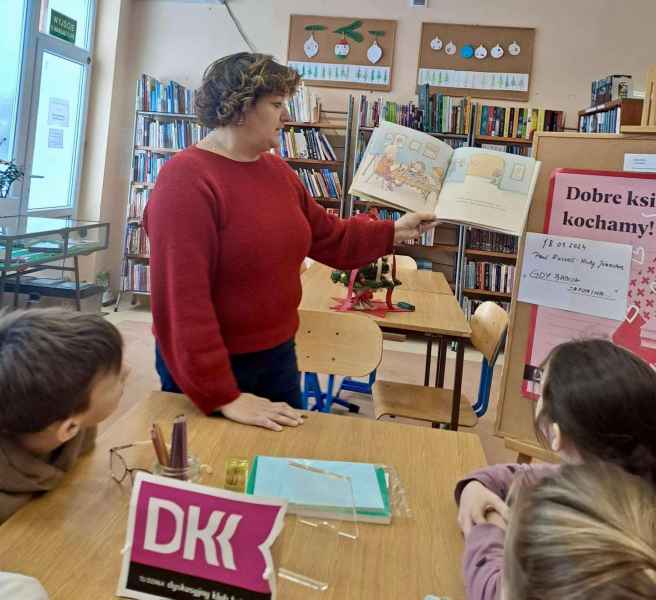 zdjęcie bibliotekarki pokazującej dzieciom ilustracje w książce