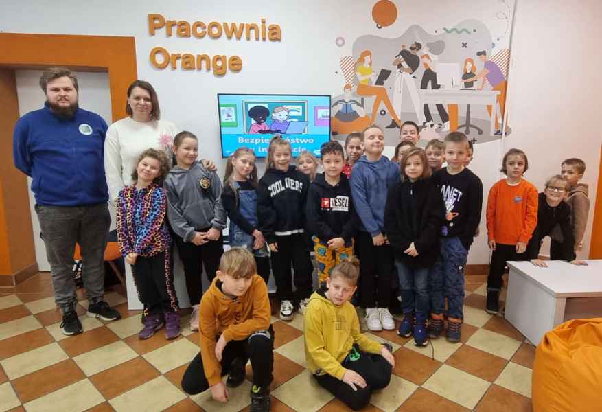 zdjęcie klasy 2b wraz z wychowawcą i informatykiem w pracowni orange, z tyłu ekran monitora z prezentacją i napis pracownia orange