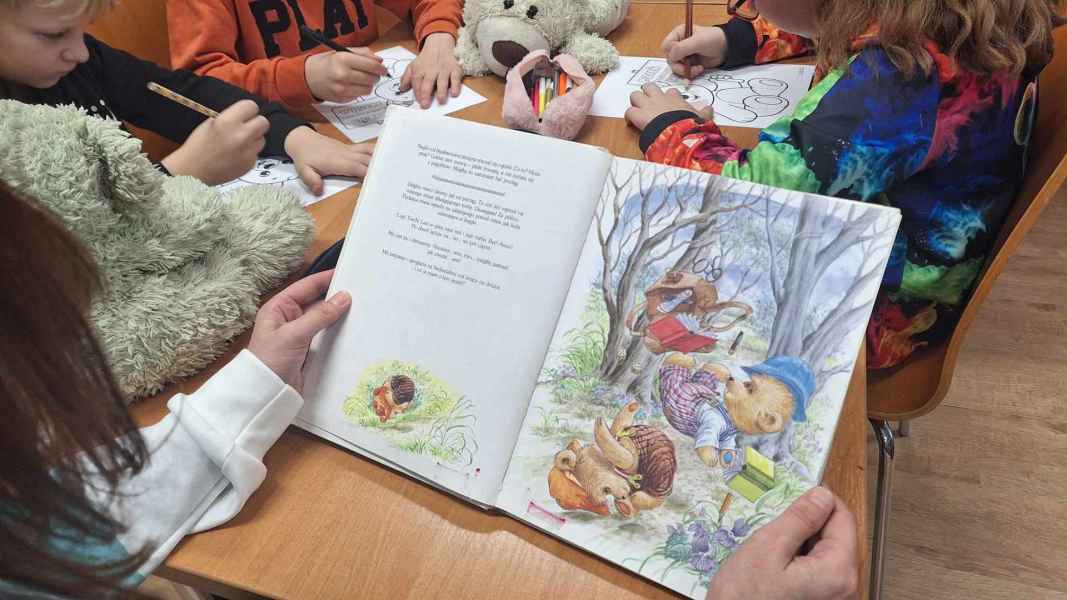 zdjęcie dziecka czytającego książkę, w tle dzieci kolorujące obrazek przy stole