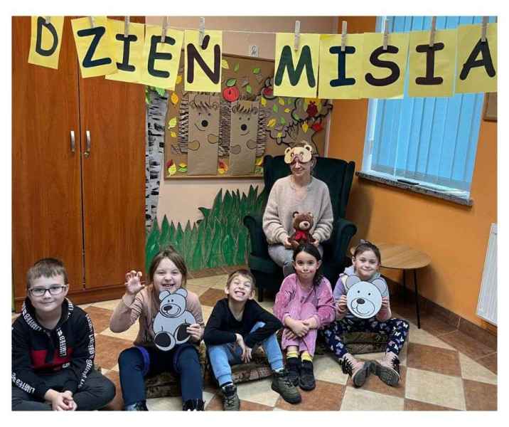 zdjęcie bibliotekarki w masce misia, przed nią dzieci na podłodze z wyciętymi rysunkami misia, nad nimi napis dzień misia