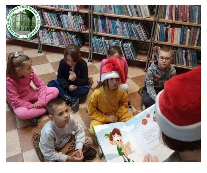 zdjęcie bibliotekarki czytającej dzieciom książkę, po lewej logo biblioteki