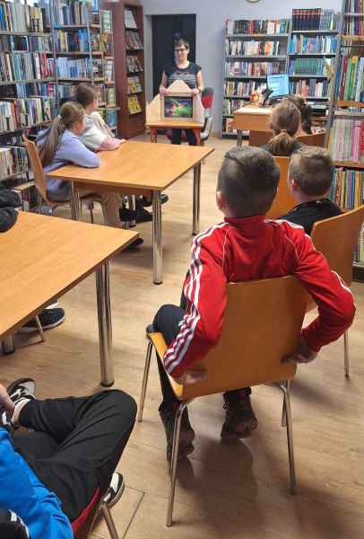 zdjęcie bibliotekarki przy teatrzyku kamishibai, na pierwszym planie dzieci przy stolikach