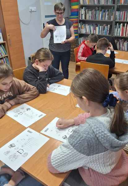 zdjęcie bibliotekarki pokazującej dzieciom zadania na kartce