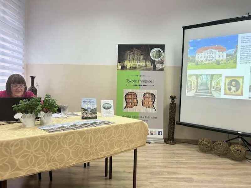 zdjęcie autorki czytającej z laptopa, w tle baner biblioteki i slajd z prezentacji ze zdjęciami