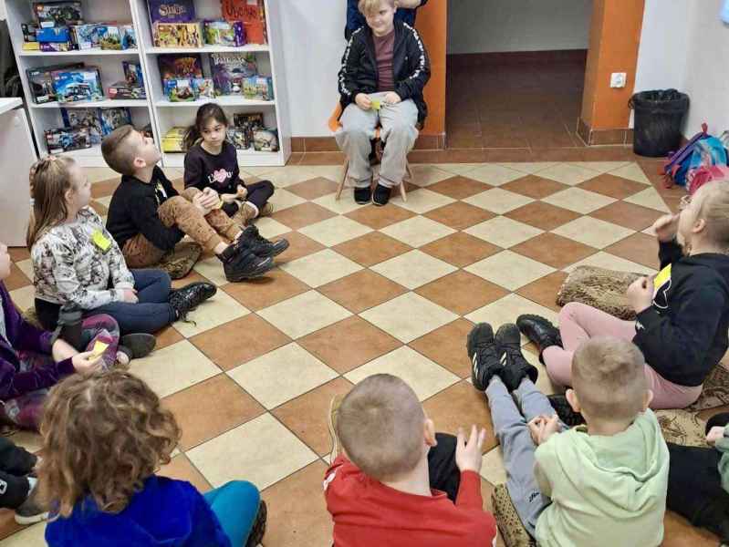 zdjęcie chłopca na krześle i obserwujących go dzieci z podłogi