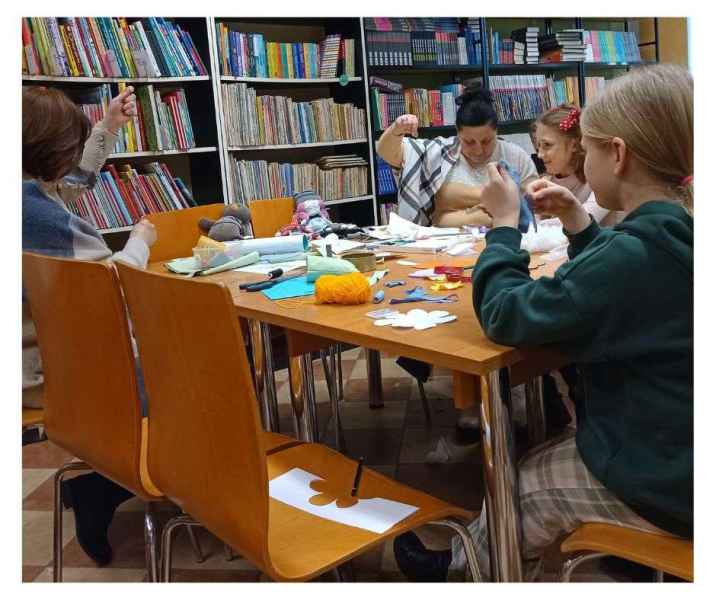 zdjęcie bibliotekarki i czytelników przy stoliku podczas szycia