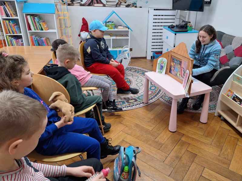 zdjęcie bibliotekarki i dzieci podczas prezentacji teatrzyku kamishibai