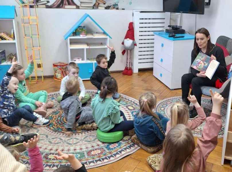 zjęcie bibliotekarki pokazującej dzieciom książkę i zgłaszające się przedszkolaki