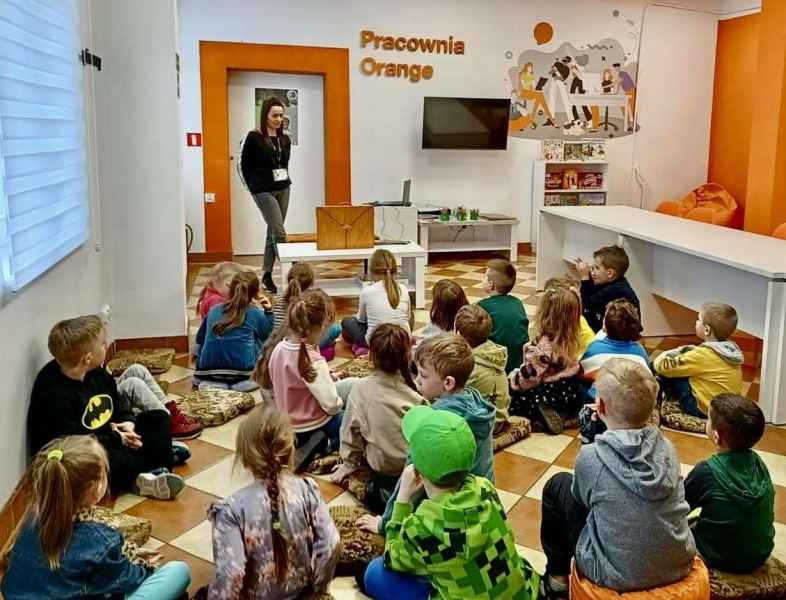 zdjęcie bibliotekarki mówiącej do dzieci siedzących na pufach na podłodze