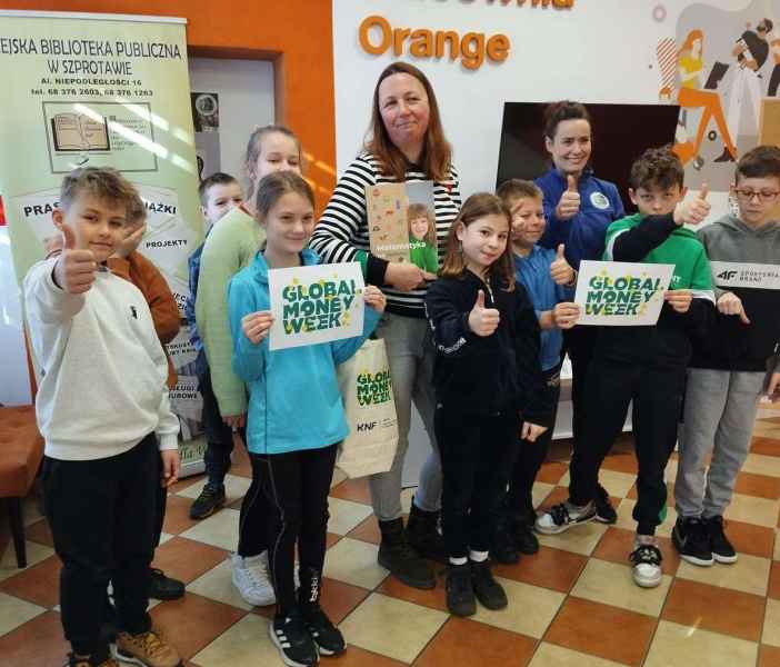 grupowe zdjęcie bibliotekarki z dziećmi i wychowawczynią z kartkami z logo projektu global money week