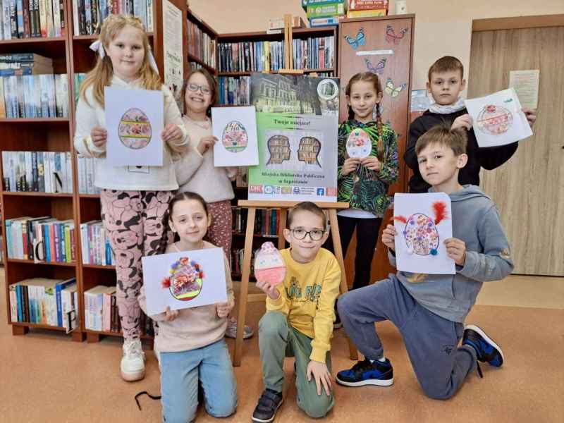 zdjęcie dzieci przy plakacie biblioteki z wykonanymi pracami pisanek na papierze