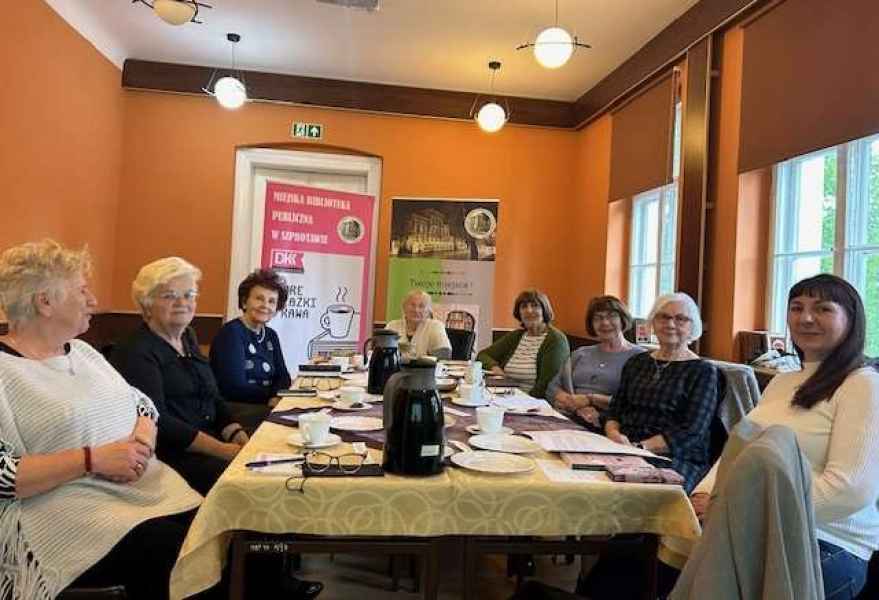 zdjęcie czytelniczek z bibliotekarką przy stoliku i banery projektu DKK i biblioteki