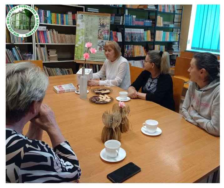 zdjęcie pań przy stoliku podczas opowiadania o doświadczeniach, po lewej logo biblioteki