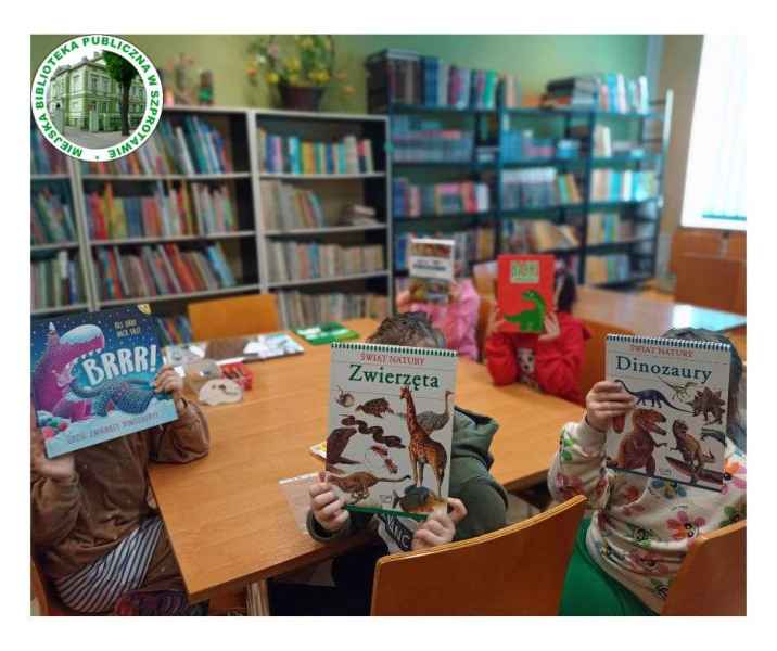 zdjęcie dzieci z książkami o dinozaurach na wysokości twarzy, po lewej logo biblioteki