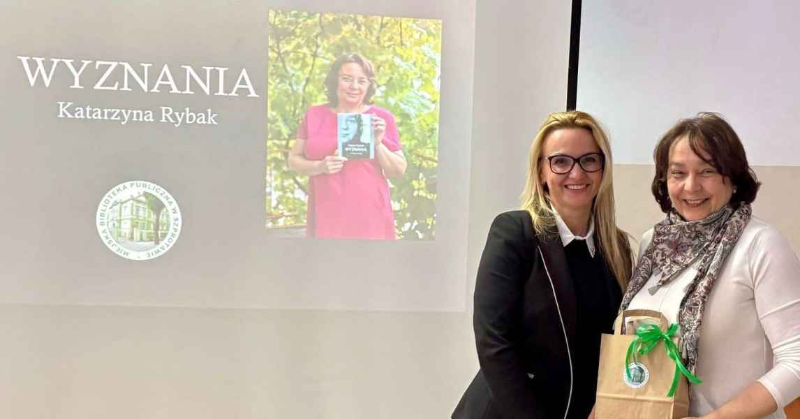 zdjęcie dyrektor biblioteki z pisarką podczas wręczenia upominku na tle prezentacji o książce pisarki