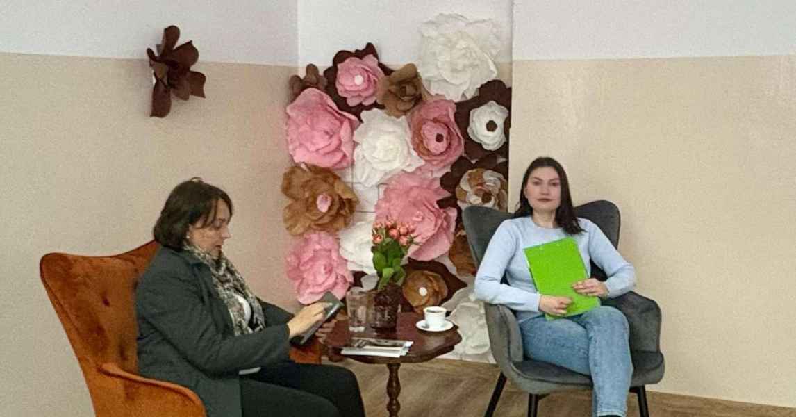 zdjęcie pisarki oraz prowadzącej w fotelach, w tle ściana ozdobiona kwiatami z papieru