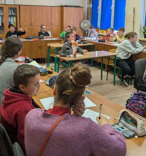 zdjęcie dzieci przy stolikach podczas słuchania bibliotekarki