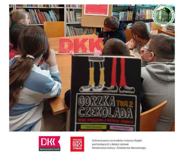zdjęcie odwróconych tyłem dzieci przy stoliku, z przodu książka gorzka czekolada tom 2, po prawej logo biblioteki, na dole logo DKK, instytutu książki i informacja o dofinansowaniu ze środków instytutu książki