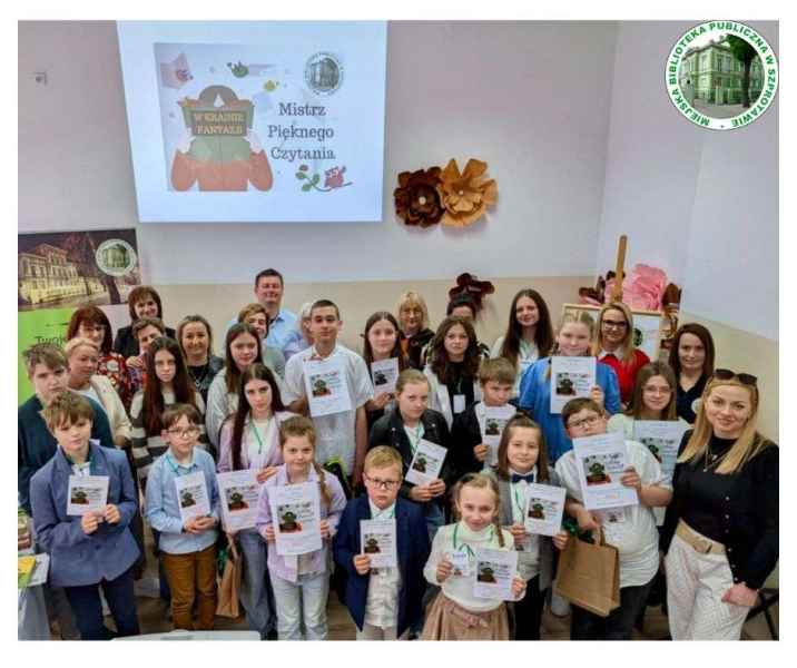 grupowe zdjęcie wszystkich uczestników wraz z jury, po prawej logo biblioteki