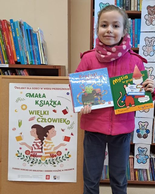 zdjęcie czytelniczki z książką wyprawką czytelniczą i plakatem projektu